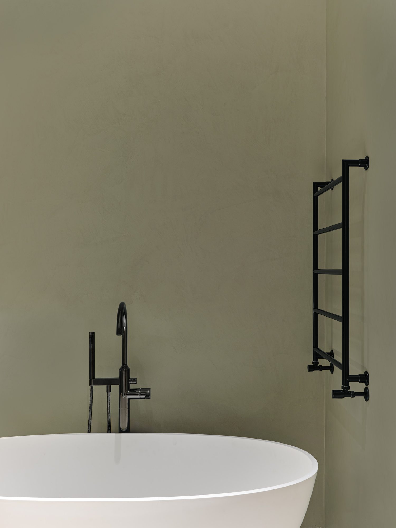 Bathroom wall in Micro-Quartz microcement, a continuous olive-toned surface running behind a freestanding bath